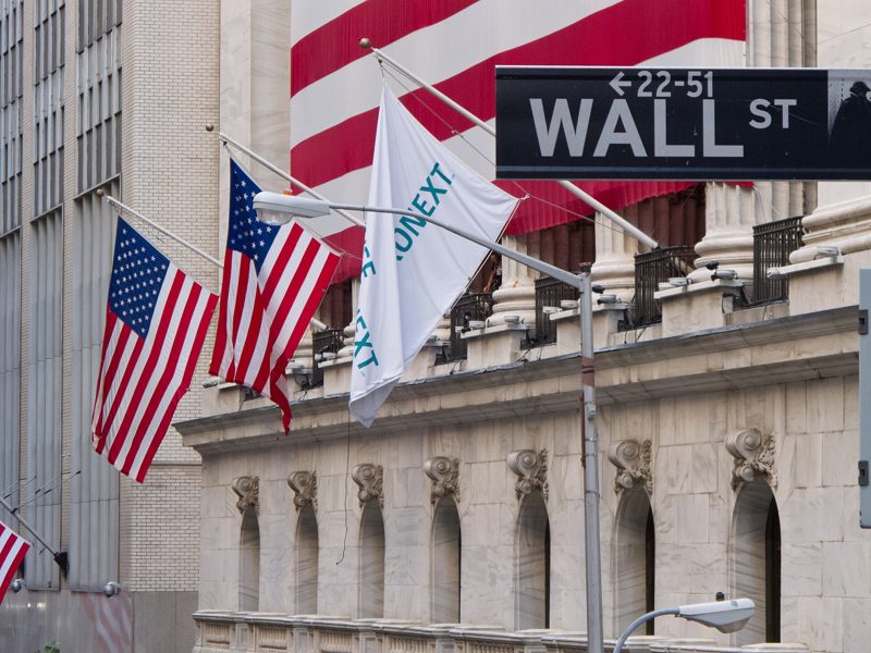 American flags hanging outside the New York Stock Exchange beside a Wall St sign
