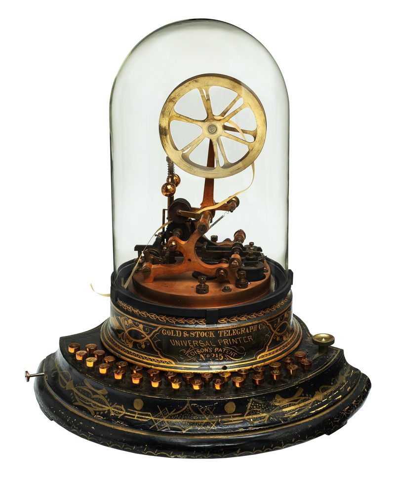 A brass stock ticker machine under a glass dome