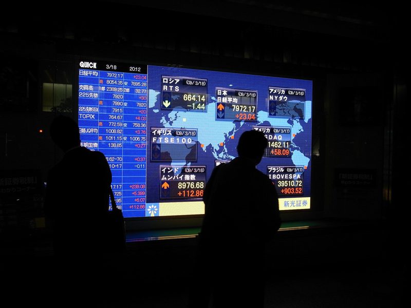 Silhouetted people in front of a glowing stock board at night