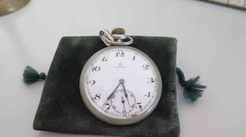 A silver pocket watch lying on a green velvet pouch